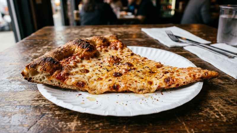Fresh hot cheese slice of New York style pizza on a paper plate.