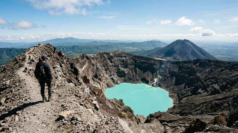 Hiker looking down at the stunning turquoise crater lake of Santa Ana Volcano in El Salvador.