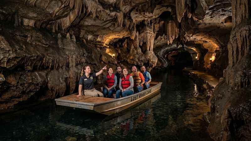 Tourists on a flat-bottom boat gliding through the illuminated limestone waters of Lost River Cave.