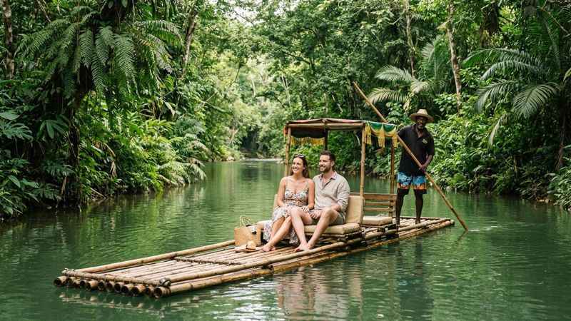 A guide steering a bamboo raft carrying tourists down the lush Martha Brae River near Montego Bay.
