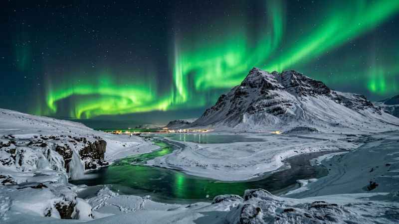 Brilliant green Northern Lights illuminating the night sky over a snowy winter landscape in Iceland.