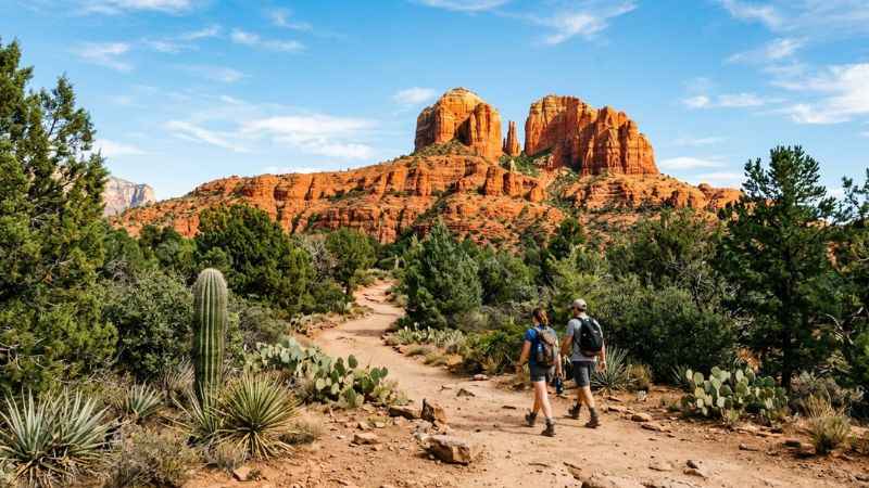 Hikers walking along a dusty trail surrounded by red sandstone rocks in Sedona, Arizona.
