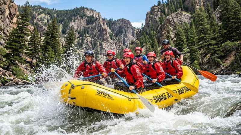 Adventurers whitewater rafting through the deep canyon walls of the Snake River in Jackson Hole, Wyoming.