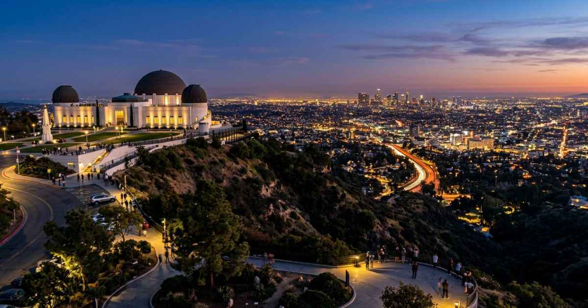 Griffith Observatory perched on a hill overlooking the glowing Los Angeles skyline at dusk.