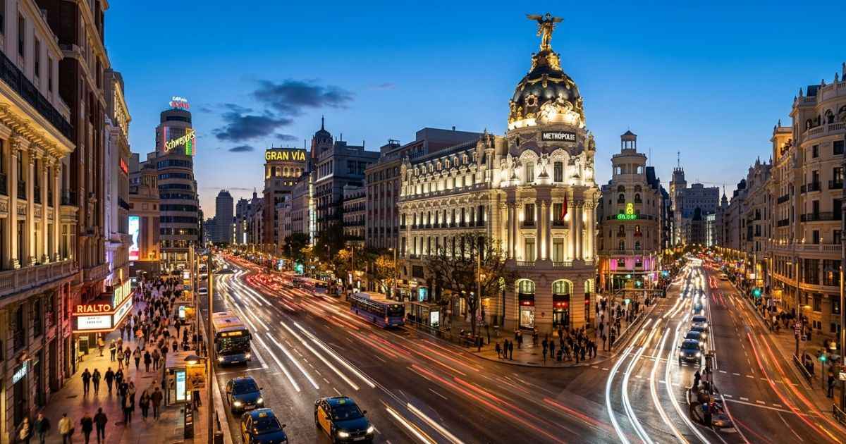 Illuminated buildings along Gran Vía avenue in downtown Madrid at dusk.