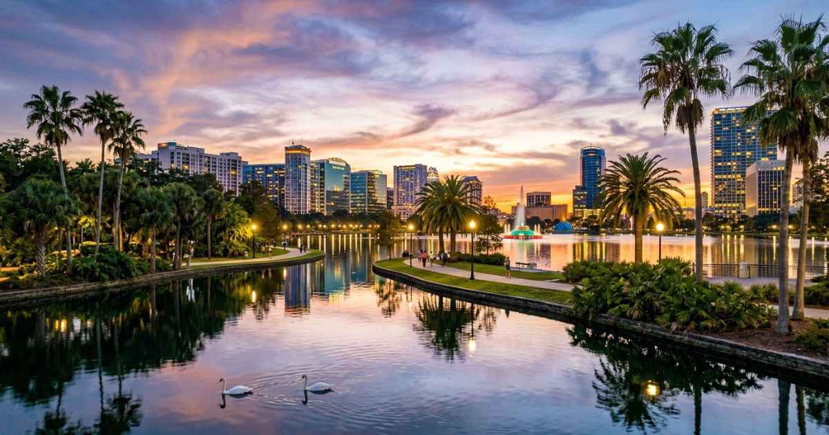 Orlando skyline reflected on Lake Eola at sunset with palm trees and calm waters.