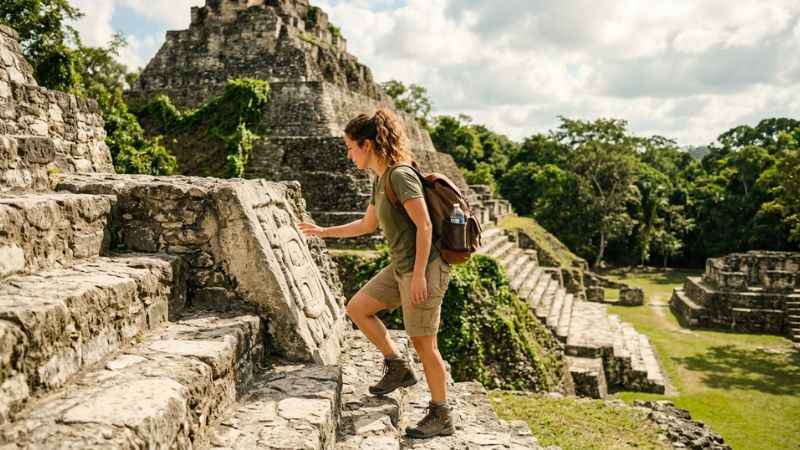 Tourist exploring El Castillo pyramid at Xunantunich archaeological site in Belize.