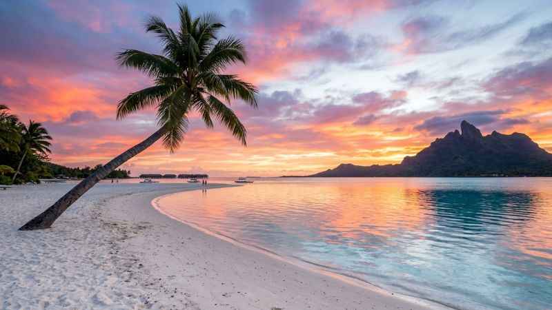 Golden sunset casting warm light over the white sand and shallow water of Matira Beach in Bora Bora.