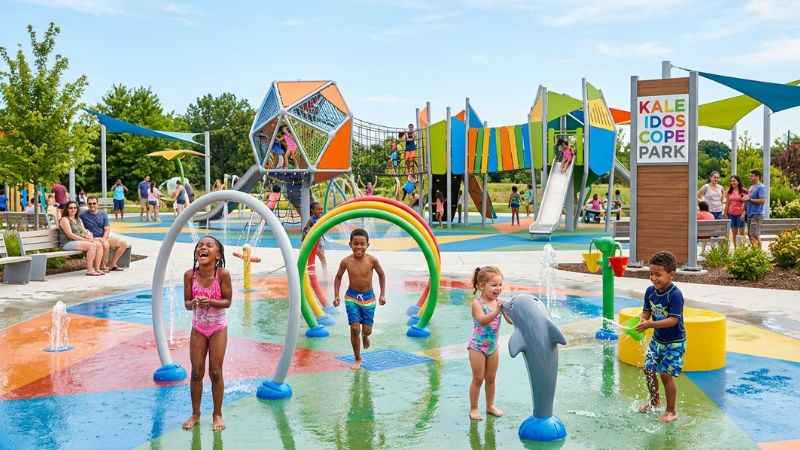 Families enjoying the splash pad and public art installations at Kaleidoscope Park in Frisco.