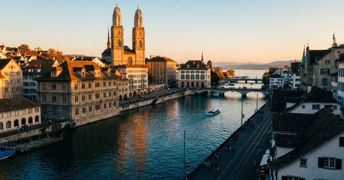 Panoramic view of Zurich Old Town and Grossmünster towers along the Limmat River at sunset.